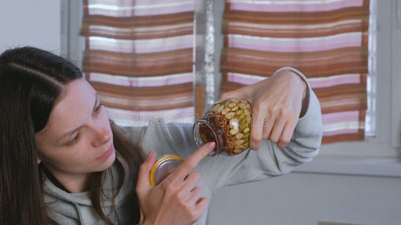 Frau, die Honig von einem Glas Nüssen im Honig mit dem Finger isst