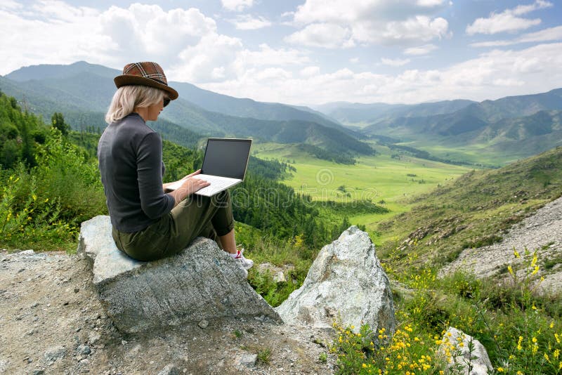 Woman working on her computer on the top of the mountain. Remote work concept. Woman working on her computer on the top of the mountain. Remote work concept