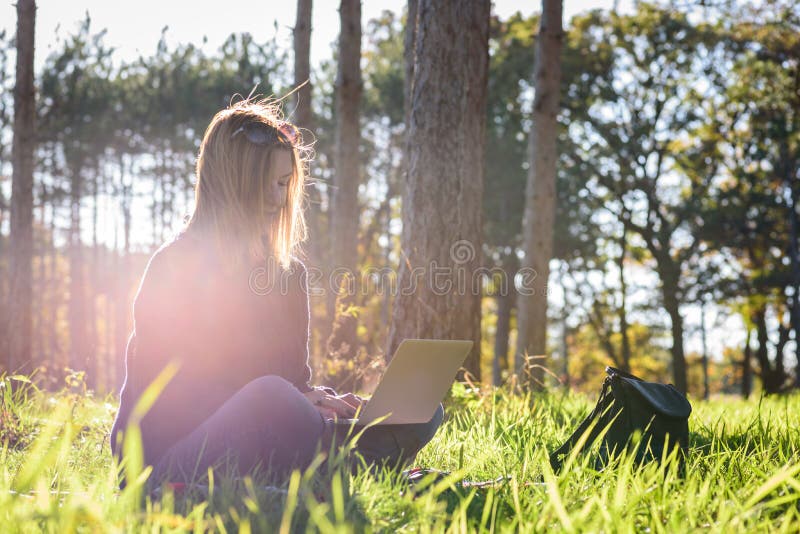 Frau, die im Wald mit dem Laptop genießt Sonne des späten Nachmittages sitzt lizenzfreie stockfotos Frau, die im Wald mit dem Laptop genießt Sonne des späten Nachmittages sitzt lizenzfreie stockfotos