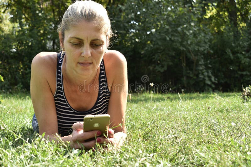 Frau, die intelligentes Mobiltelefon im Park verwendet stockbild Frau, die intelligentes Mobiltelefon im Park verwendet stockbild