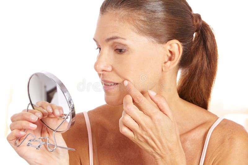 Elderly woman looking for wrinkles around the corner of her mouth in mirror. Elderly woman looking for wrinkles around the corner of her mouth in mirror