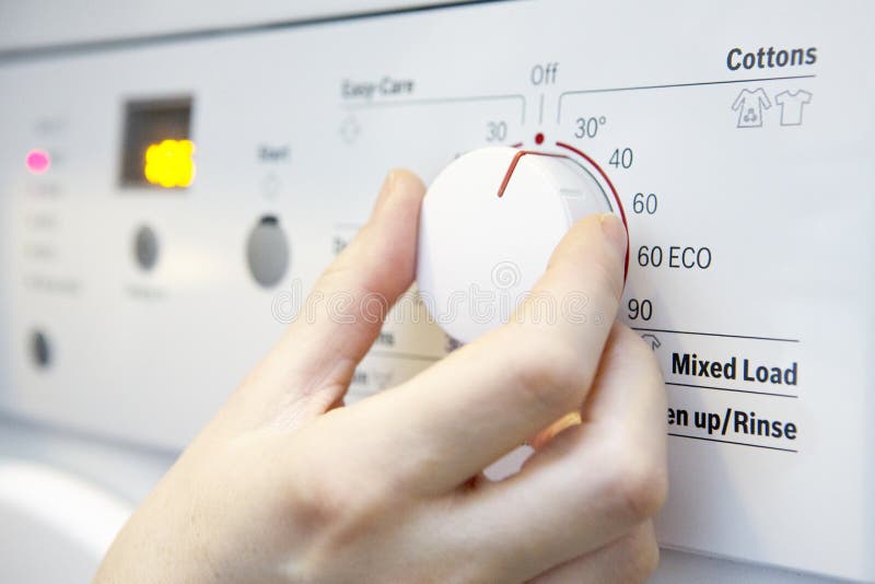 Frau, die kühlere Temperatur auf Waschmaschine vorwählt, um en zu sparen stockfotografie
