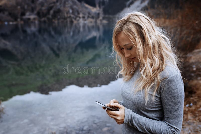 Frau, die Smartphone am See verwendet lizenzfreie stockbilder