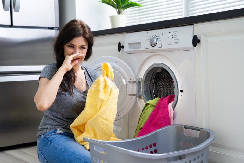 Frau, die stinkende Kleidung aus Waschmaschine aus betrachtet stockfotografie