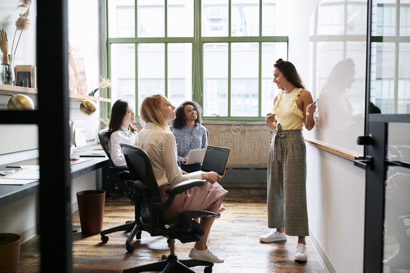 Frau, die am whiteboard in einer Sitzung mit weiblichem Team steht stockbild