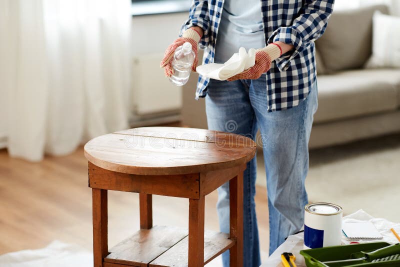 furniture renovation, diy and home improvement concept - close up of woman degreasing old round wooden table surface with solvent and paper. furniture renovation, diy and home improvement concept - close up of woman degreasing old round wooden table surface with solvent and paper