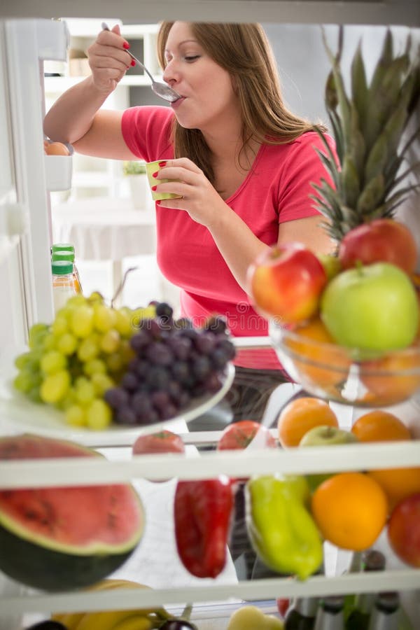 Frau essen Fruchtjoghurt vom Kühlschrank lizenzfreie stockbilder Frau essen Fruchtjoghurt vom Kühlschrank lizenzfreie stockbilder