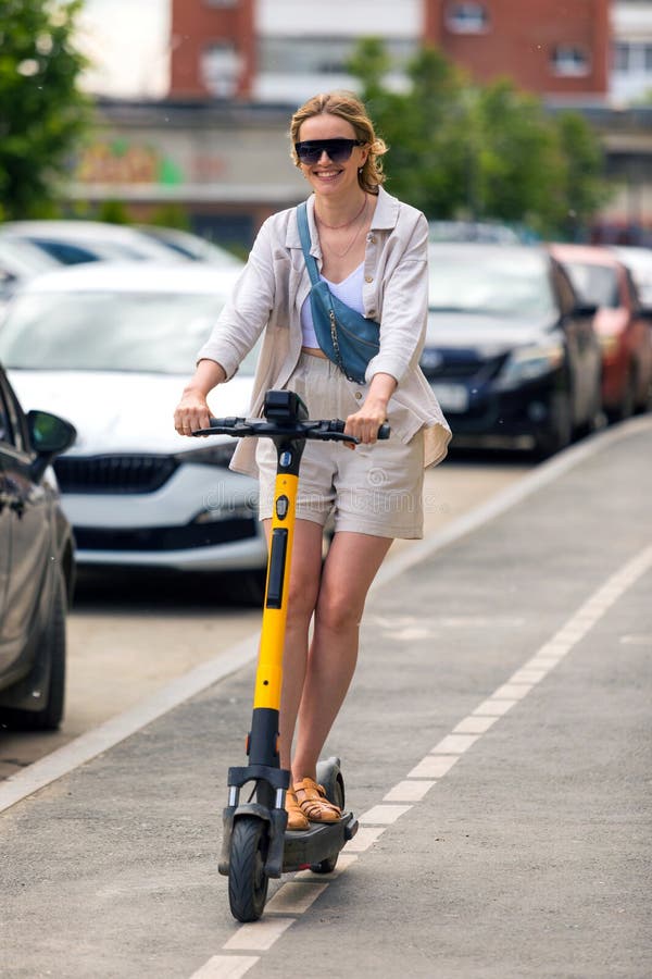 Frau fährt auf einem Elektroroller auf einer Stadtstraße lizenzfreies stockfoto