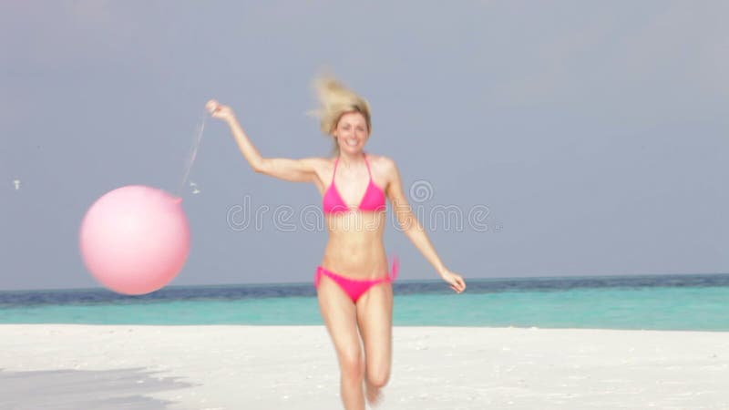 Frau im Bikini, der auf schönem Strand mit Ballon läuft