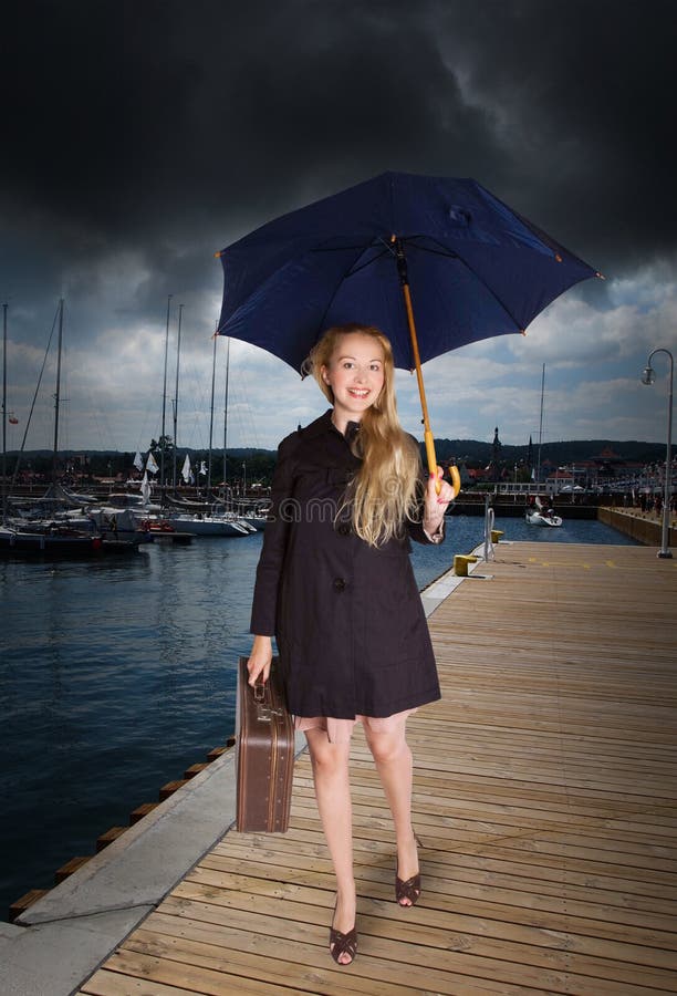 Frau mit altem Koffer und Regenschirm am Hafen stockbild Frau mit altem Koffer und Regenschirm am Hafen stockbild