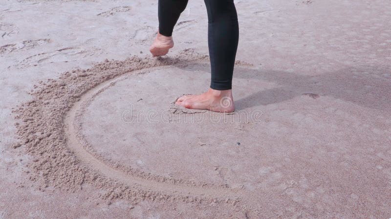 Frau mit den bloßen Füßen, die Kreis auf Sand nahe Meer zeichnen