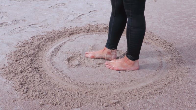 Frau mit den bloßen Füßen, die smiley auf Sand nahe Meer zeichnen