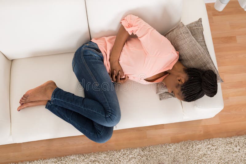 High Angle View Of Young African Woman With Stomach Ache Lying On Sofa. High Angle View Of Young African Woman With Stomach Ache Lying On Sofa