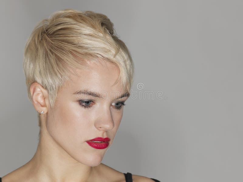 Closeup of beautiful young woman with red lips looking down on gray background. Closeup of beautiful young woman with red lips looking down on gray background