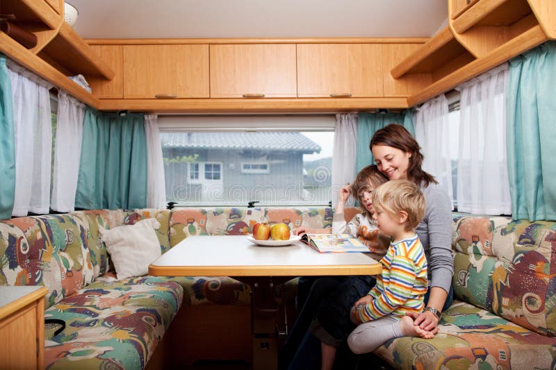 Frau mit den Söhnen, die bei Tisch Geschichten-Buch im Wohnwagen lesen lizenzfreies stockfoto Frau mit den Söhnen, die bei Tisch Geschichten-Buch im Wohnwagen lesen lizenzfreies stockfoto