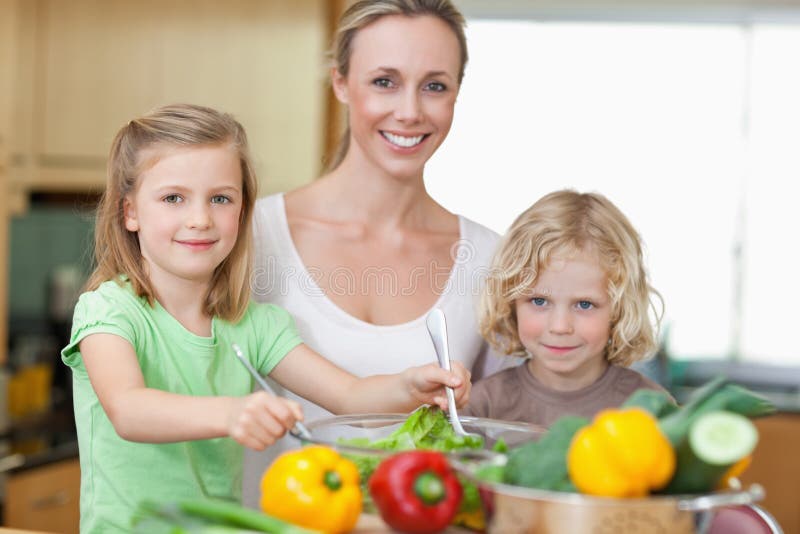 Frau mit ihren Kindern, die Salat zubereiten