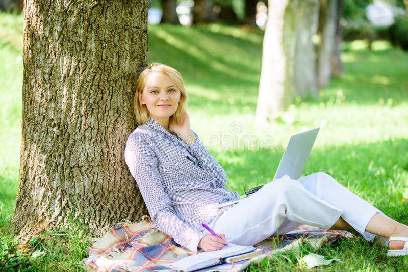 Woman with laptop computer work outdoors lean on tree trunk. Girl work with laptop in park sit on grass. Education technology and internet concept. Natural environment office. Work outdoors benefits. Woman with laptop computer work outdoors lean on tree trunk. Girl work with laptop in park sit on grass. Education technology and internet concept. Natural environment office. Work outdoors benefits.