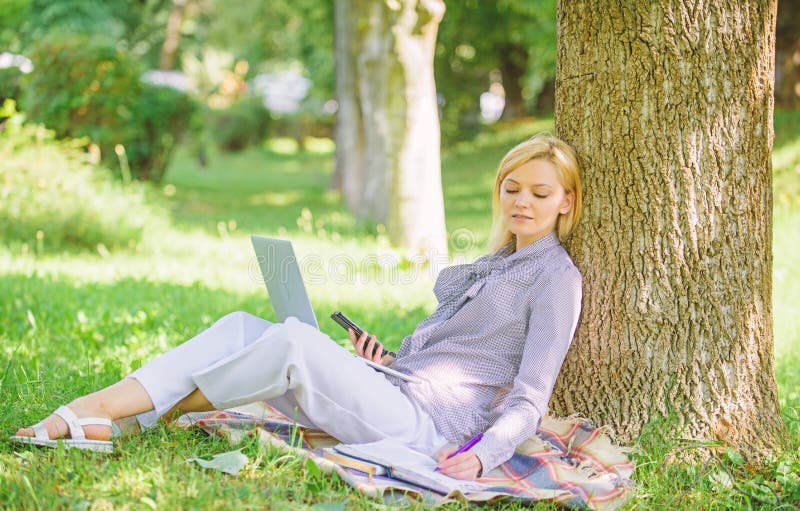 Woman with laptop computer work outdoors lean on tree trunk. Girl work with laptop in park sit on grass. Natural environment office. Work outdoors benefits. Education technology and internet concept. Woman with laptop computer work outdoors lean on tree trunk. Girl work with laptop in park sit on grass. Natural environment office. Work outdoors benefits. Education technology and internet concept.