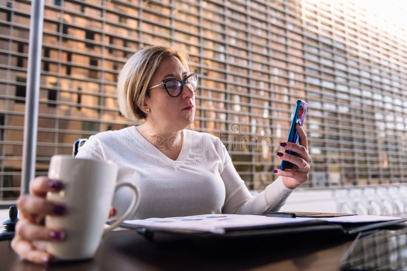 Frau mit Mobiltelefon, die auf einer Terrasse sitzt lizenzfreies stockfoto