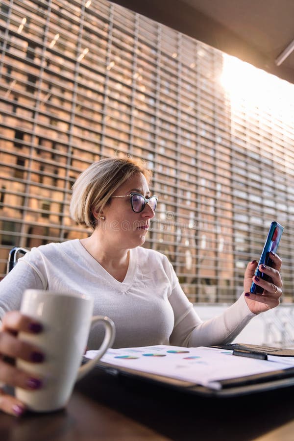 Frau mit Mobiltelefon, die auf einer Terrasse sitzt stockbilder