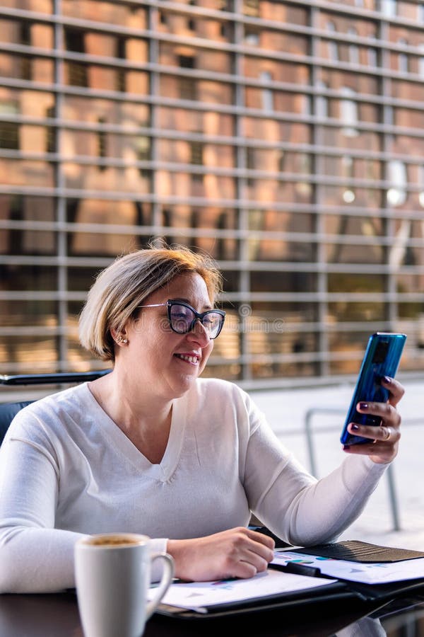 Frau mit Mobiltelefon, die auf einer Terrasse sitzt lizenzfreie stockfotos