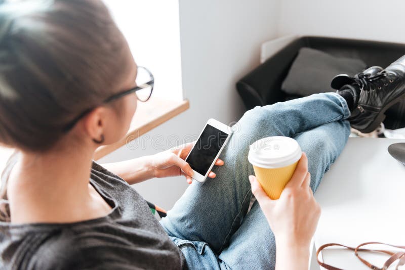 Frau mit Tasse Kaffee-Sitzen und mit Handy stockfotografie Frau mit Tasse Kaffee-Sitzen und mit Handy stockfotografie