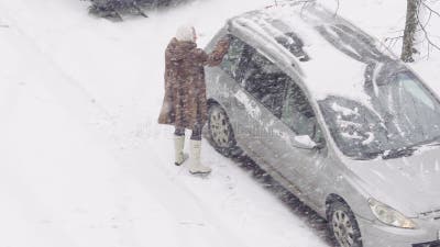 Ein Mann reinigt ein Auto von Schnee mit einem Besen