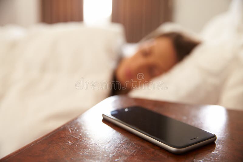 Frau schlafend im Bett mit Handy auf Nachttisch lizenzfreies stockbild Frau schlafend im Bett mit Handy auf Nachttisch lizenzfreies stockbild