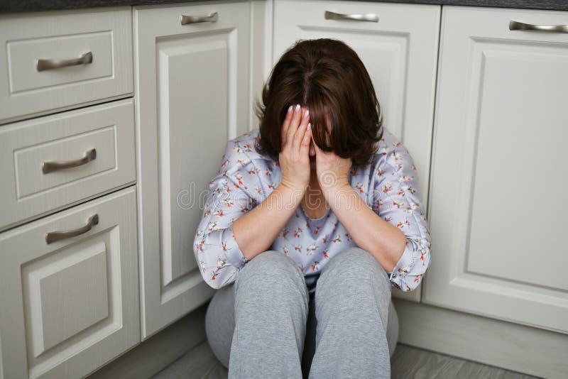 Frau sitzt auf Küchenfußbodenbelag ihr Gesicht mit ihren Händen Krise, Leid oder Frustration