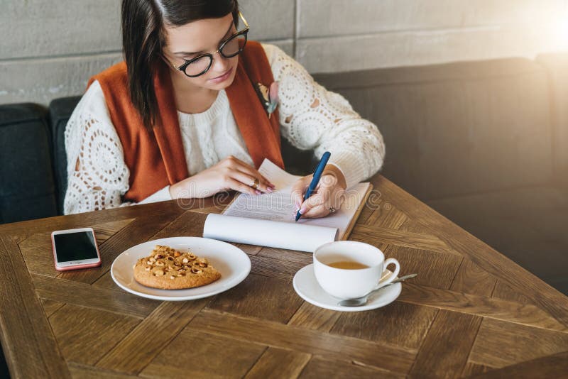 Frau sitzt im Café bei Tisch und arbeitet Mädchen ergänzt eine Anwendung, Zeichendokumente, aufstellt Zusammenfassung lizenzfreie stockfotografie Frau sitzt im Café bei Tisch und arbeitet Mädchen ergänzt eine Anwendung, Zeichendokumente, aufstellt Zusammenfassung lizenzfreie stockfotografie