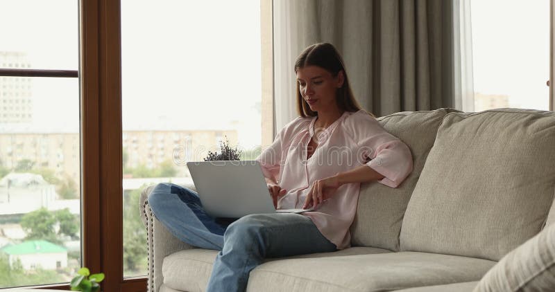 Frau sitzt zu Hause auf Sofa und tippt auf der Tastatur des Laptops