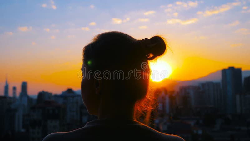 Frau steht auf dem Balkon und schaut auf den Sonnenaufgang