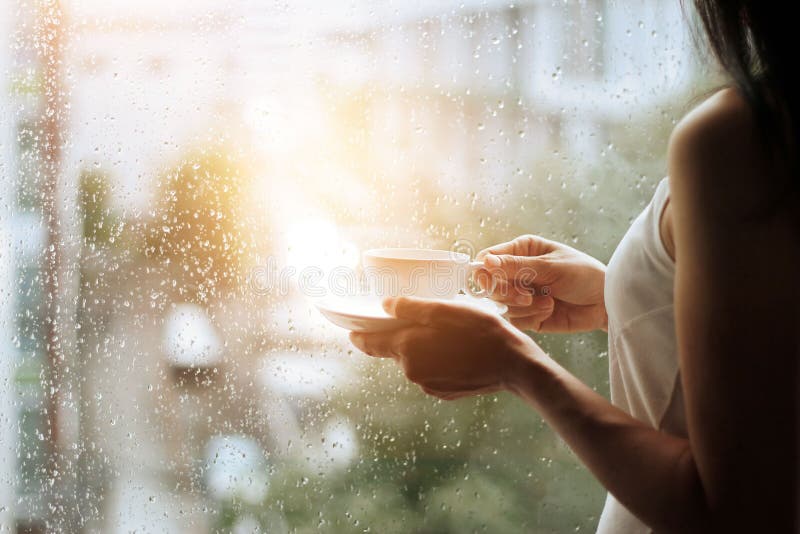 Frau und Kaffeetasse in den Händen, die durch Glasfenster schauen lizenzfreie stockbilder Frau und Kaffeetasse in den Händen, die durch Glasfenster schauen lizenzfreie stockbilder