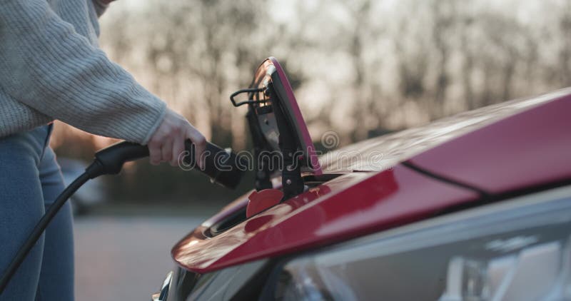 Frau verstopft Elektrofahrzeuge für die Erhebung der Autobatterie am Parken. Aufladungselektroauto. ev Auto Verbindung