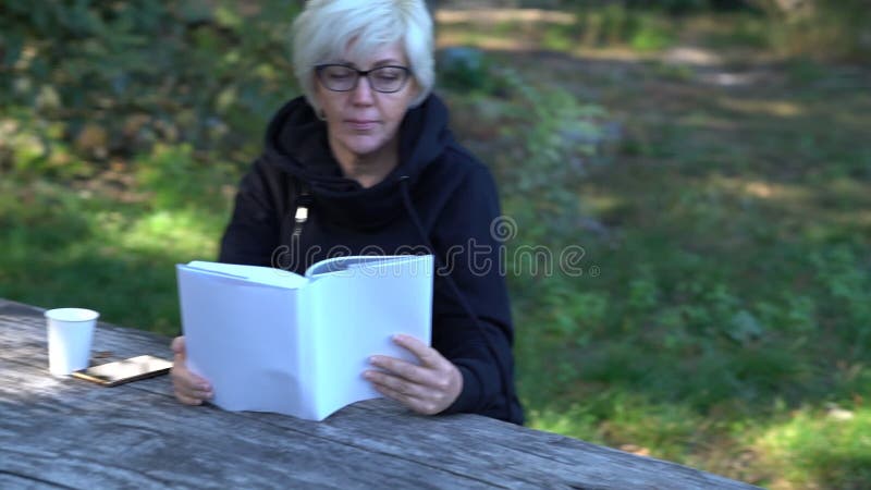 Frau von mittlerem Alter, die ein Buch im Wald liest