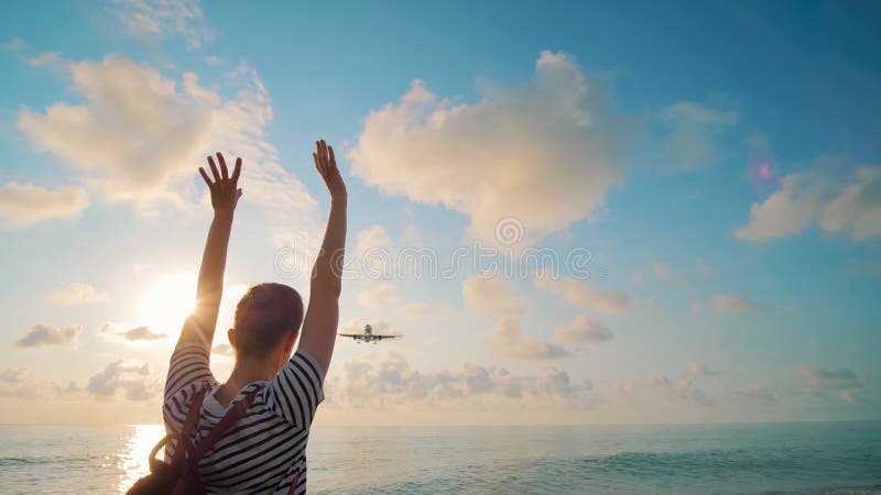 Frau Wellen Arme trifft das ankommende Flugzeug gegen den Himmel bei Sonnenuntergang