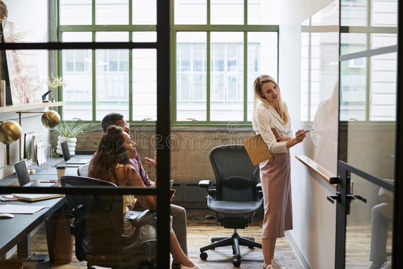 Frau am whiteboard in der Teambesprechung, gesehene durch offene Tür stockfotografie