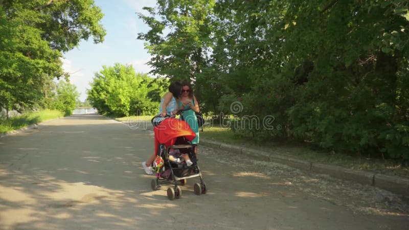 2 Frauen betrachten den Handy, während das Baby im Spaziergänger schläft