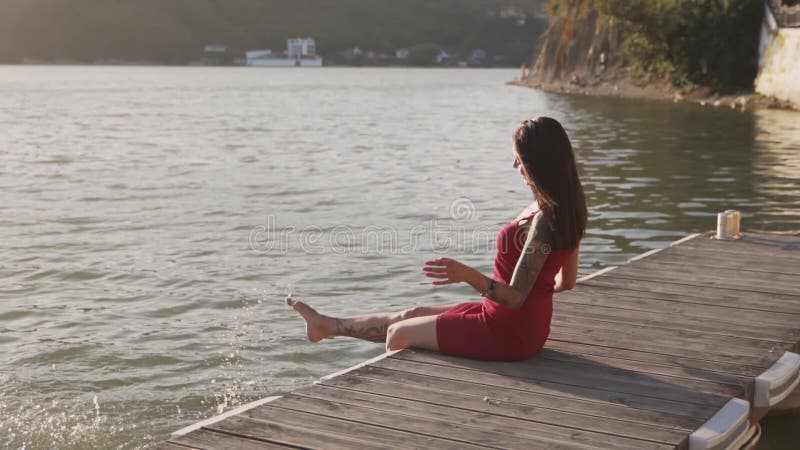 Frauen, die auf Holzsteg sitzen, mit ihren Füßen im Seenwasser spritzen, Zeitlupe