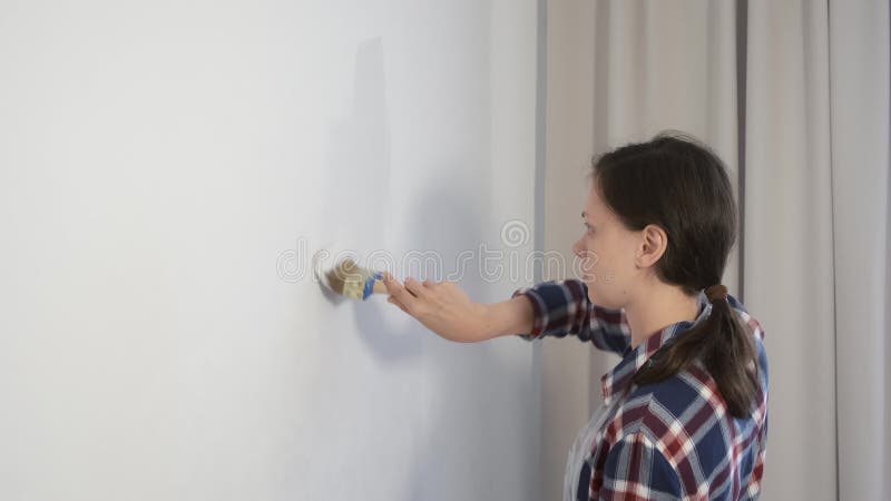 Frauenanstreicher zeichnet Mauer mithilfe der Pinsel zu Hause Erneuerung wird.