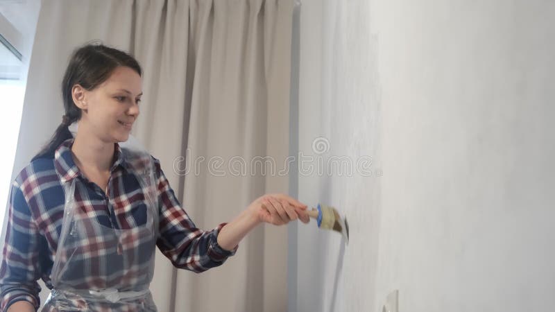 Frauenanstreicher zeichnet Mauer mithilfe der Pinsel zu Hause Erneuerung wird.