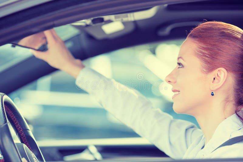 Frauenfahrer, der Autospiegel der hinteren Ansicht justierend schaut lizenzfreie stockfotos Frauenfahrer, der Autospiegel der hinteren Ansicht justierend schaut lizenzfreie stockfotos