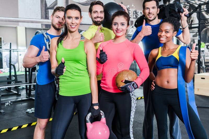 Group of women and men in gym posing at fitness training standing together with gear and dumbbells. Group of women and men in gym posing at fitness training standing together with gear and dumbbells