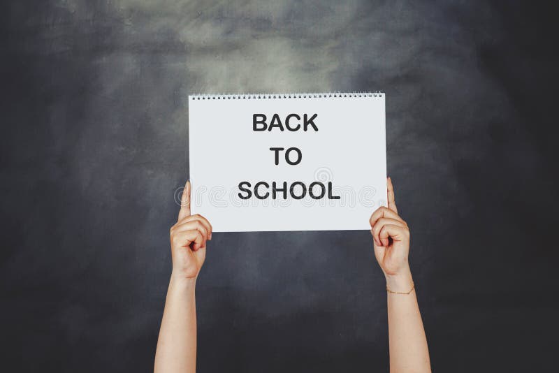 Frauenhände, die hoch eine Postkarte halten, die ZURÜCK ZU SCHULE gegen eine Tafel sagt stockfoto Frauenhände, die hoch eine Postkarte halten, die ZURÜCK ZU SCHULE gegen eine Tafel sagt stockfoto