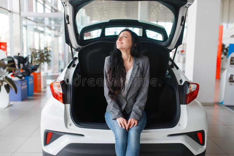 Woman buying new car in showroom, lady near the opened trunk. Female customers choosing vehicle in dealership, automobile sale, auto purchase. Woman buying new car in showroom, lady near the opened trunk. Female customers choosing vehicle in dealership, automobile sale, auto purchase
