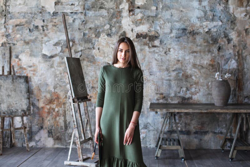 Frauenmaler in einem grünen Kleid mit einer Bürste und einer Palette fotografiert in einem Kunststudio lizenzfreie stockfotos Frauenmaler in einem grünen Kleid mit einer Bürste und einer Palette fotografiert in einem Kunststudio lizenzfreie stockfotos