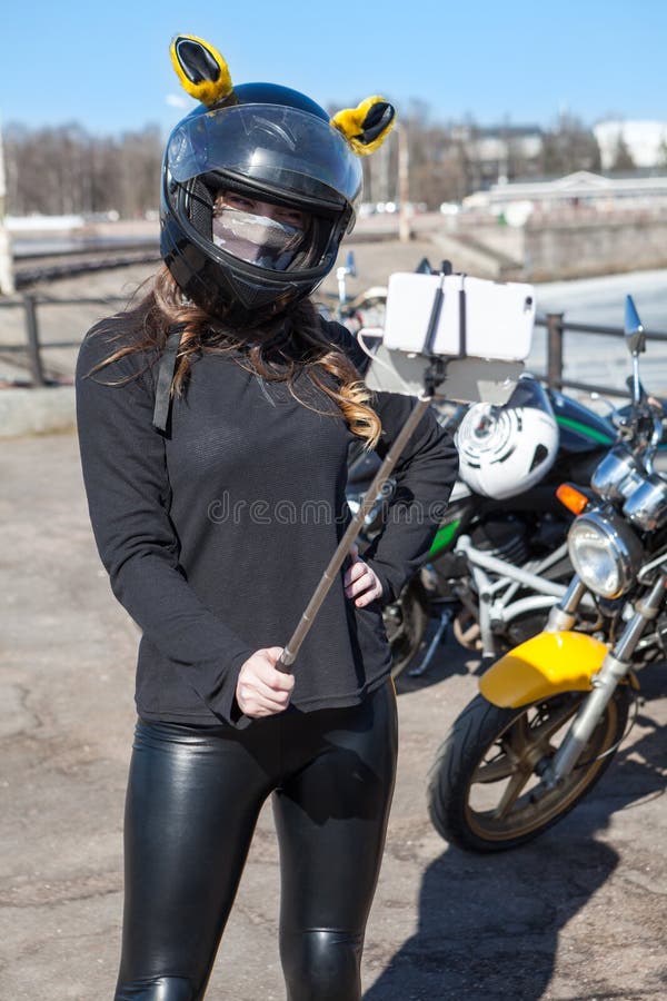 Frauenmotorradfahrer im Sturzhelm mit den Ohren, die selfies unter Verwendung des Mobiltelefons mit dehnbarem monopod nehmen lizenzfreies stockbild Frauenmotorradfahrer im Sturzhelm mit den Ohren, die selfies unter Verwendung des Mobiltelefons mit dehnbarem monopod nehmen lizenzfreies stockbild