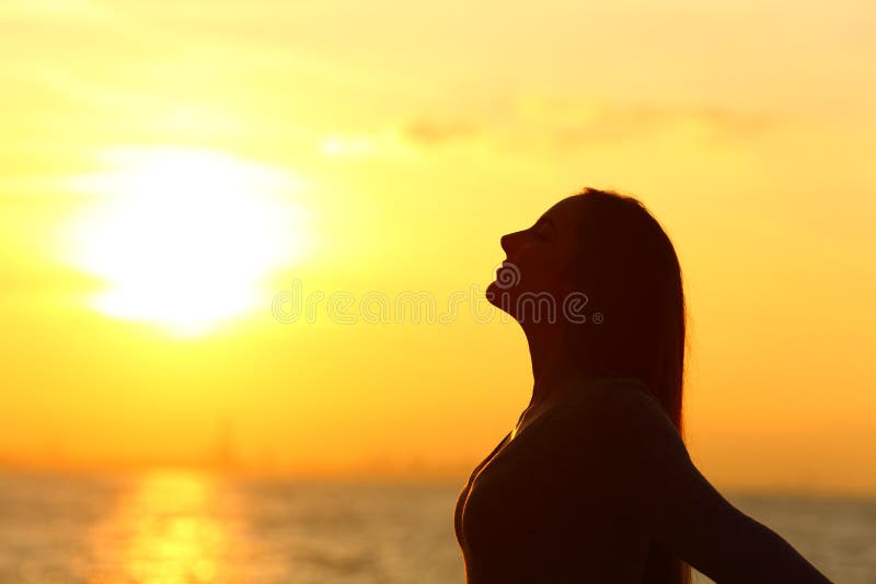 Side view portrait of a relaxed woman silhouette breathing fresh air at sunset on the beach. Side view portrait of a relaxed woman silhouette breathing fresh air at sunset on the beach