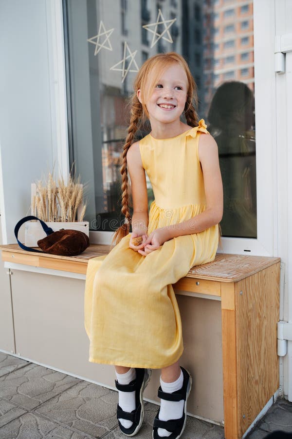 Freckled ginger girl is sitting on a bench. Feet hanging in the air.