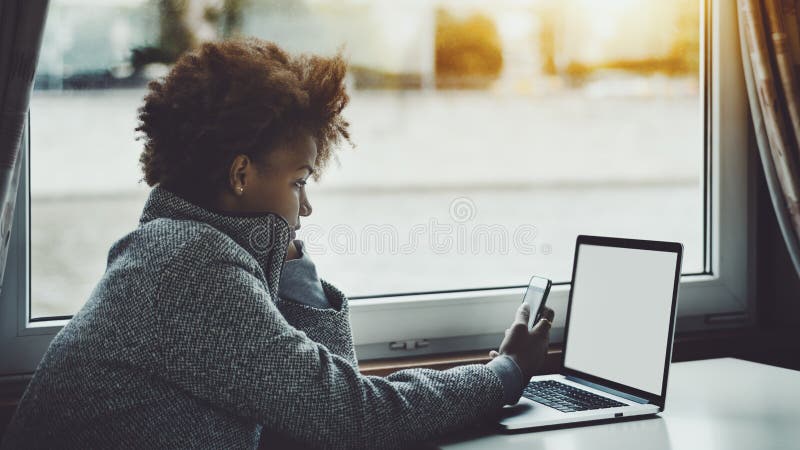 Free lance ricce nere con il computer portatile e lo smartphone fotografia stock libera da diritti Free lance ricce nere con il computer portatile e lo smartphone fotografia stock libera da diritti